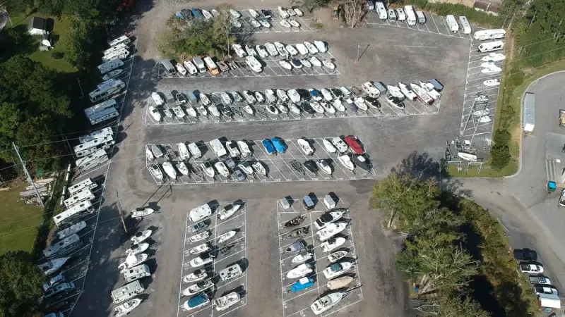 Storage Lot Layout A parking lot filled with various boats, showcasing different sizes and colors, under bright sunlight.